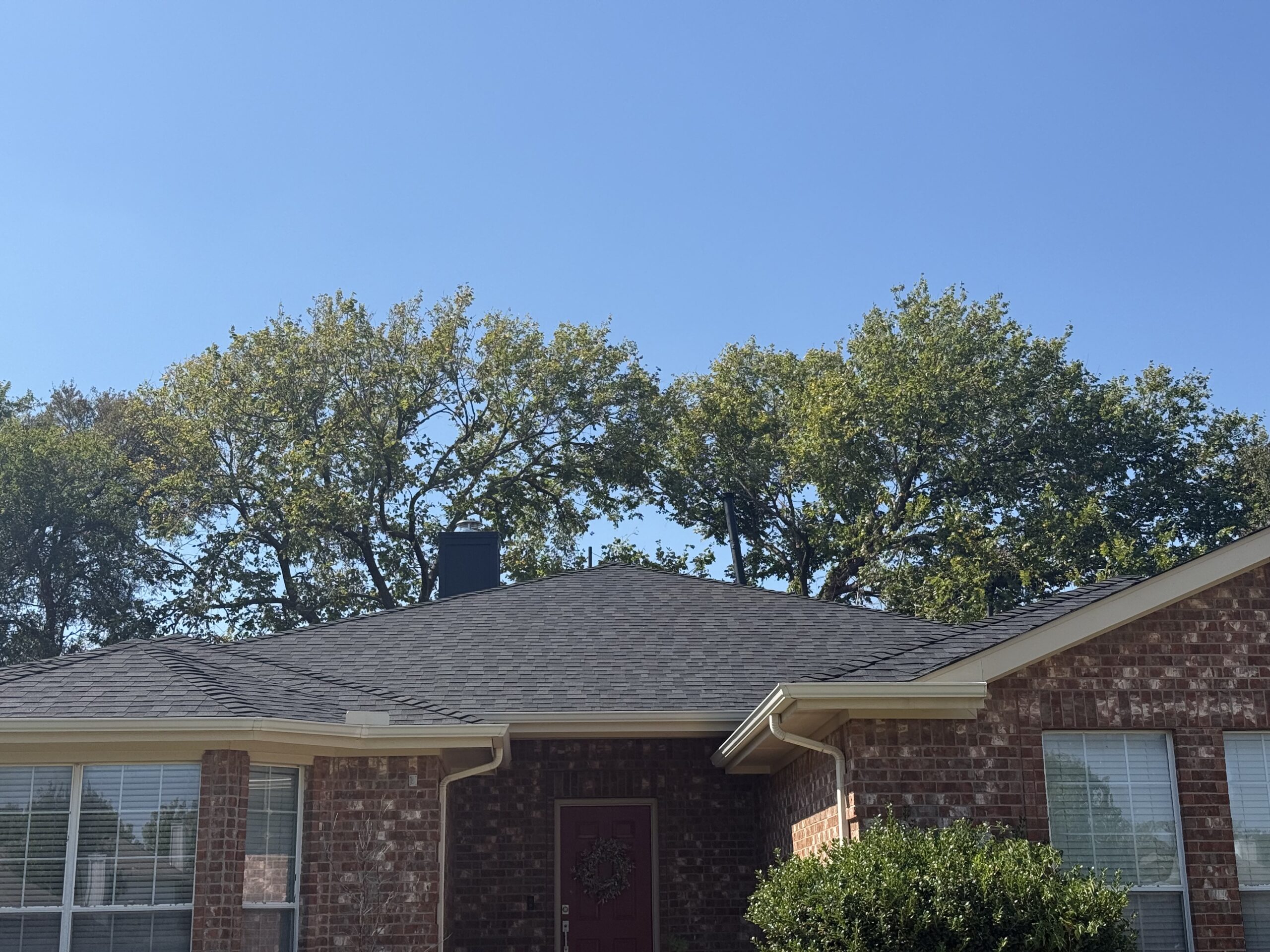 Closer front view of a completed asphalt shingle roof on a brick home